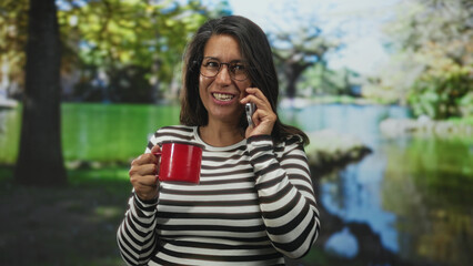 Woman middle age brunette wearing glasses and striped sweater, holding a red mug and talking on a...