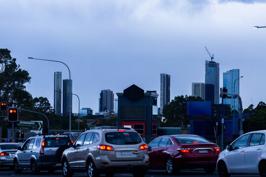 Busy city road with traffic stopping at lights at dusk red tail lights on and skyscrapers on horizon