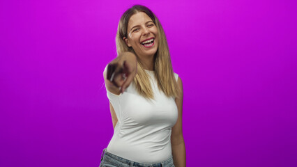 Fototapeta premium Woman points finger at camera laughing and leaning forward in studio with vibrant magenta backdrop; playful confidence.
