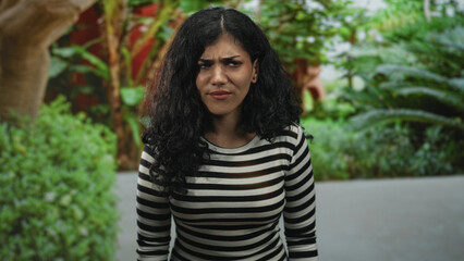 Naklejka premium Woman in striped top looks up, head tilted amid green foliage in a forest setting, relaxed posture and natural expression; quiet contemplation.