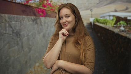 Obraz premium Young woman with hand on chin leaning against a stone wall on an urban street; thoughtful introspection.