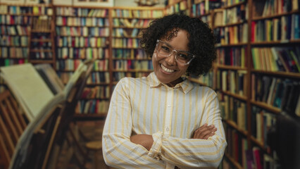 Woman wearing glasses with arms crossed smiling in a historic library with rows of bookshelves and a wooden bookstand  confidence. © Krakenimages.com