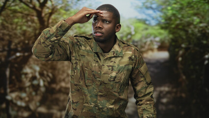 Obraz premium Soldier man shading hand to forehead while scanning a forest path for threats on patrol; vigilance duty.