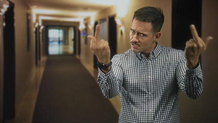 Hispanic man with moustache grimaces while showing middle fingers and a visible wristwatch in a dim...