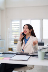 Obraz premium Asian adult businesswoman talks smartphone smiling office desk communication professional cheerful female happy remote work modern workplace technology mobile call advisor