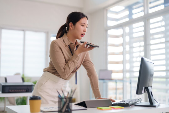 Asian business professional woman uses voice command smartphone dictating message communicating efficient task management online work modern corporate office environment workspace