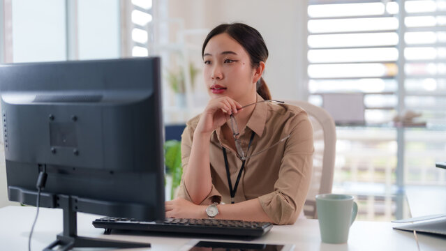 Asian adult woman professional working concentrating computer monitor office desk modern workspace business environment analyzing data focus