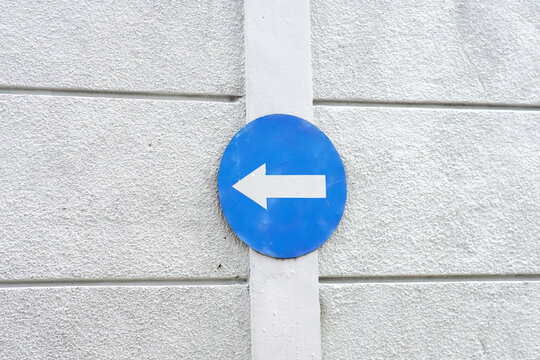 Blue directional sign with white arrow on concrete wall