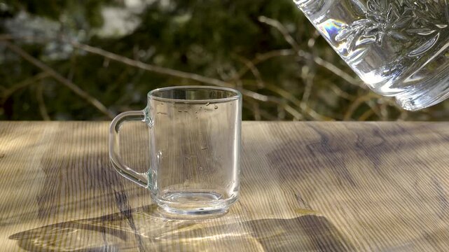 Refreshing water pouring into glass mug with windy nature background, 4K 120fps.