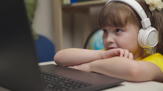 little schoolgirl headphones does homework while sitting digital laptop. distance learning online students. children funny communication through internet video communication. lessons monitor display