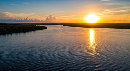 Fototapeta premium Aerial view of a wide river reflecting a vibrant sunset over lush green forest