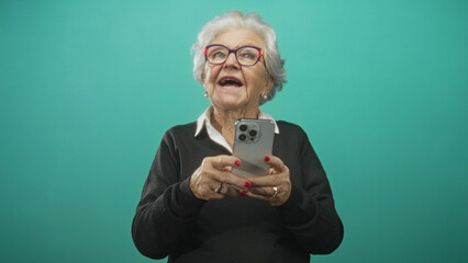 Fototapeta premium Senior woman holds smartphone with visible hands, mouth open and looking up in a studio; joyful curiosity.
