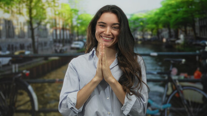 Fototapeta premium Woman smiling crosses fingers on bridge over canal on an urban street with bicycle rack in view; hope.