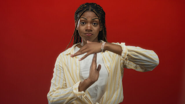Woman showing timeout sign with hands in red studio, braided hair and bracelet visible; boundary setting assertive.