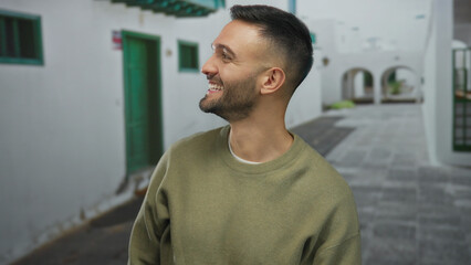 Smiling man in casual attire stands on a narrow street in an old town, capturing a lively moment in an urban outdoor setting, evoking a cheerful vibe. © Krakenimages.com