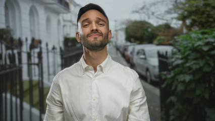 Young man in white shirt stands outdoors on an urban street with closed eyes, expressing a peaceful emotion amid city surroundings, blending with modern architecture and greenery. © Krakenimages.com