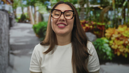 Woman wearing glasses stands smiling with visible face under sunlight in a green park surrounded by trees  serenity. © Krakenimages.com