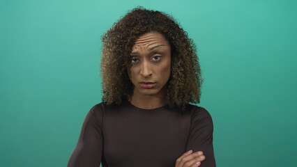 Transgender woman with curly brown hair and hoop earrings crosses arms firmly in studio setting  rejection defiance. © Krakenimages.com