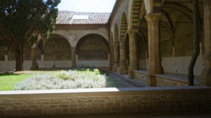 Fototapeta premium Historic cloister courtyard with arched colonnade and leafy garden in soft blurred focus, defocused; background backdrop copyspace template.