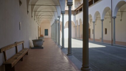 Arched cloister corridor with columned arcade, terracotta floor and bench, softly blurred shallow focus; background backdrop copyspace calm.