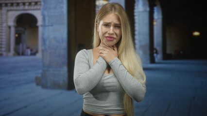 Fototapeta premium Woman clutching her neck with both hands in a stone archway building, choking and showing worried expression; distress fear vulnerability.