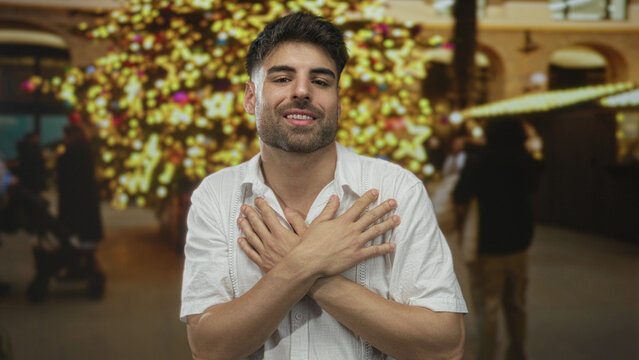 Young man crosses hands over chest on street near christmas tree lights in city market; self acceptance confidence.