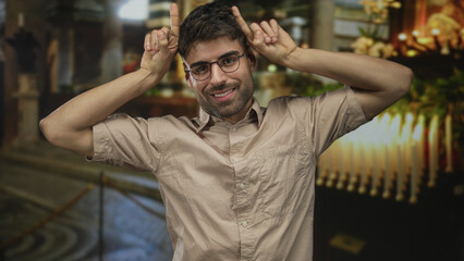 Fototapeta premium Young hispanic man showing rock horns with hands in church building; playful energy youthful spirit.