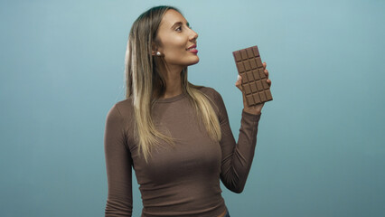 Woman holding a large chocolate bar upright while looking up in a light blue studio  pleasure craving enjoyment. © Krakenimages.com