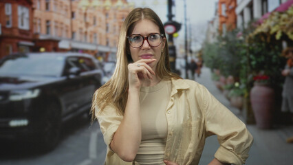Woman wearing glasses stands with finger to chin pose on busy urban street with blurred car and planter in view  reflection doubt pondering concern. © Krakenimages.com