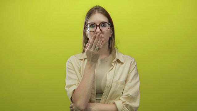 Young woman with glasses shows open mouth gesture and bare midriff in green studio setting; surprise.