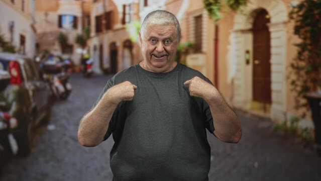 Man points both index fingers to chest in a narrow cobblestone street with parked cars and doorway, making an accusatory gesture toward himself; defiance self assertion.