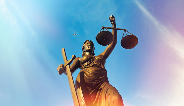 Lady Justice Statue Low Angle View with Sunlight Flare Against Blue Sky
