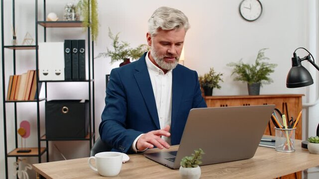 Middle-aged businessman at home office hammers laptop keys system stalled urgently presses restart praying recovery. Freelancer guy at table hopes reboot saves deadlines project files and vital data.