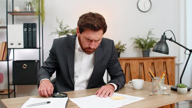 Middle-aged businessman at home office inspects contract text with magnifier finds issue and shakes head no. Freelancer guy at table writes urgent fix on sticker and places note on page to review