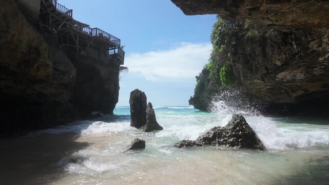 A beautiful slow motion shot of turquoise waves crashing on the sand at Suluban Beach in Uluwatu, Bali. The camera tracks forwards providing a cinematic moment of paradise. 