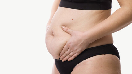 Smiling plus-size woman caressing her stomach, showing body progress. Fitness, weight loss and wellness concept.
