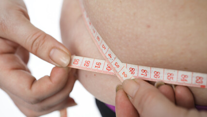 Close-up of plus-size female measuring waist after home workout. Weight loss and fitness concept.
