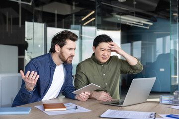 Fototapeta na wymiar Two businessmen at a modern office desk react with frustration and stress as a laptop error disrupts work, showing confusion, concern, and urgent problem-solving under deadline pressure
