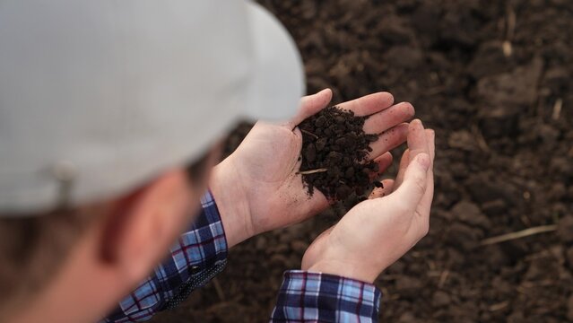 Fertile soil in male hands of farmer. Male hands hold fertile land in field. Organic soil in hands of farmer at sunset in field, natural farming. Agricultural business concept. Humus, fertilized land