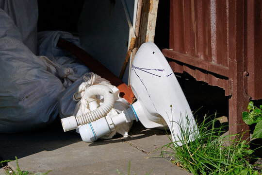 Broken ceramic sink, renovation debris and construction waste disposal. An old white bathroom sink with pipes and several heavy bags of rubble left at collection point in residential area