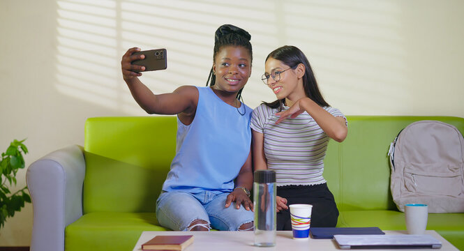 Happy young adult gen z woman sitting on sofa couch use mobile look cam take selfie indoor lounge room place teen age girl hold phone record casual video spend break time do funny pose enjoy new day