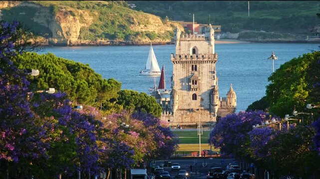Blooming jacaranda trees frame Belem Tower in Lisbon, Portugal. Tourists on boats enjoy the sunset. The flowers create a colorful view by the river, adding to the beauty of the location.