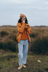 A smiling woman lifestyle enjoys nature outdoors wearing orange jacket and beanie, holding...
