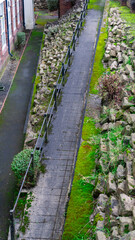 Obraz premium A ginnel a narrow pedestrian passage or alleyway between buildings. The path, paved with cobblestones or slabs, is flanked by stone boulders. View from above