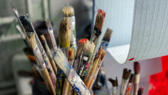 A pile of art brushes covered in paint. The brushes are standing in a tin