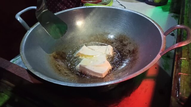Tofu is fried to golden perfection before being mixed with traditional tahu tek tek seasoning, capturing a crispy texture and the authentic street food cooking process.