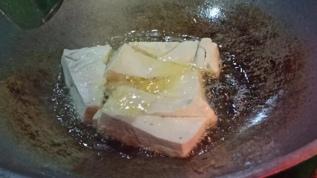 Tofu is fried to golden perfection before being mixed with traditional tahu tek tek seasoning, capturing a crispy texture and the authentic street food cooking process.