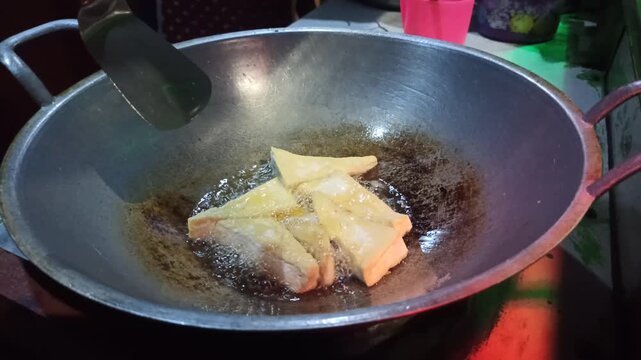 Tofu is fried to golden perfection before being mixed with traditional tahu tek tek seasoning, capturing a crispy texture and the authentic street food cooking process.