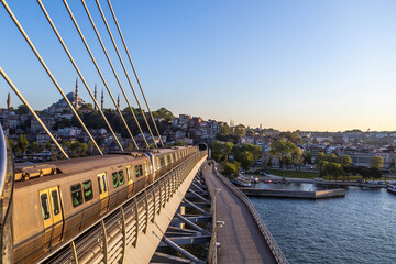 Obraz premium Modern metro train crossing Golden Horn Metro Bridge at sunset. Scenic cityscape with Suleymaniye Mosque and historical buildings on background. Urban transportation in Istanbul, Turkey.