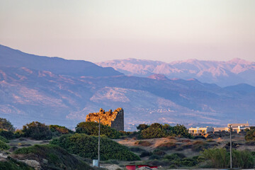 Ancient stone ruins illuminated by warm sunset light with majestic Taurus mountain range on background. Scenic landscape of historical site at twilight. Side, Antalya, Turkey.
